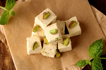 Natural vegan product. Halva with pistachios on parchment paper on a wooden background. Turkish, Arab and Jewish national sweets. Traditional oriental dessert Chekme.