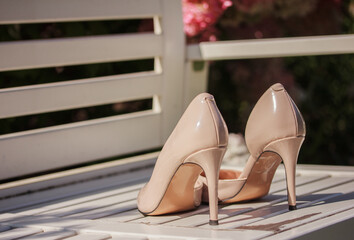White, beige high heel shoes on white wooden bank outdoors on green flowery background
