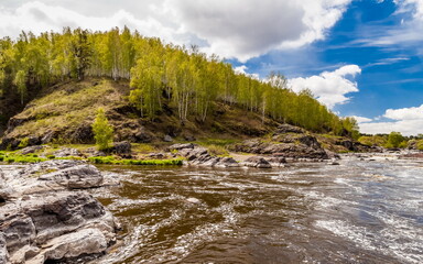 Summer landscape with fast-flowing river, stone banks, trees and blue sky with white clouds