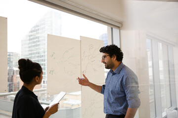 Businessman and businesswoman discussing diagram sketches hanging on conference room window