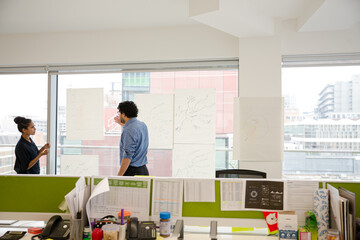 Businessman and businesswoman discussing diagram sketches hanging on conference room window