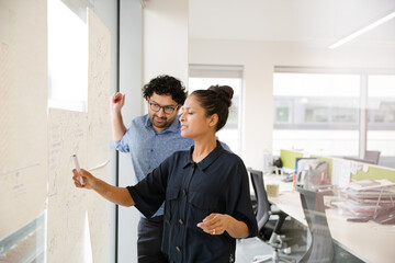 Business people discussing diagram sketches hanging on office window
