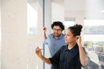 Business people discussing diagram sketches hanging on office window