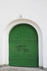 An old wrought iron door of green color in the wall of a medieval castle 