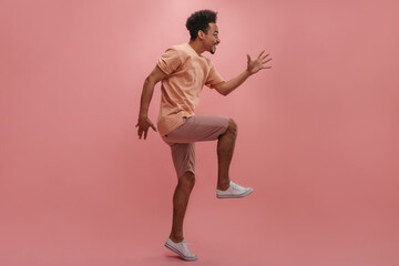 profile photo positive young man with dark skin jumping on pastel background. attractive brunette waving her arms gleefully, dressed in casual shades of pink.