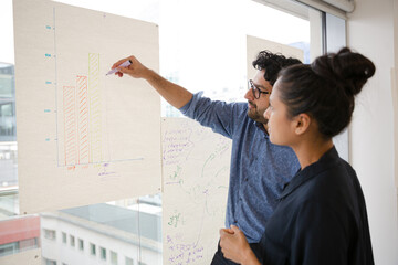Business people discussing diagram sketches hanging on office window