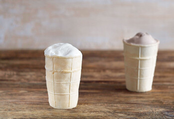 Two ice creams in a waffle cup stand on a wooden table. Clear day