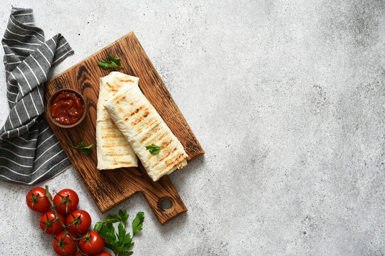 Shawarma stuffed with meat and vegetables on a wooden board against a concrete background. View from above.