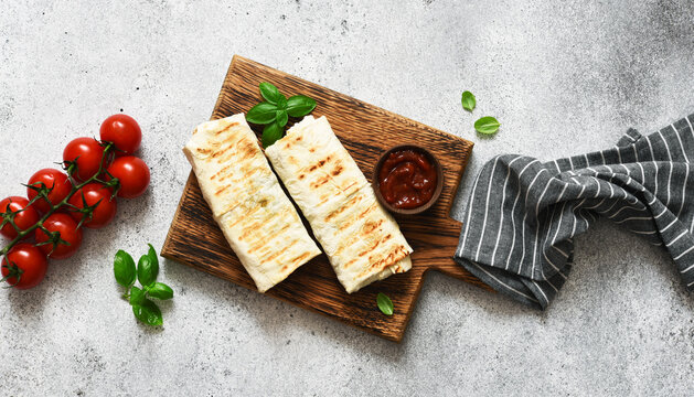 Shawarma stuffed with meat and vegetables on a wooden board against a concrete background. View from above.