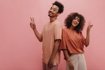 two african american friends show peace sign on pink studio background. guy and girl with dark afro...