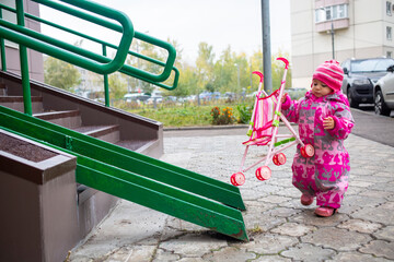 Toddler drags a toy stroller along the ramp of the stairs