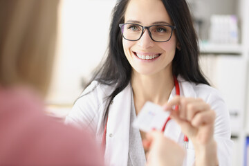 Smiling female doctor giving business card to patient at reception in clinic