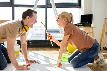 Happy young couple relaxing, painting on sheet of paper in new house on the floor, using blue and yellow colours, have fun, playing, enjoy spending time together, at home. side view