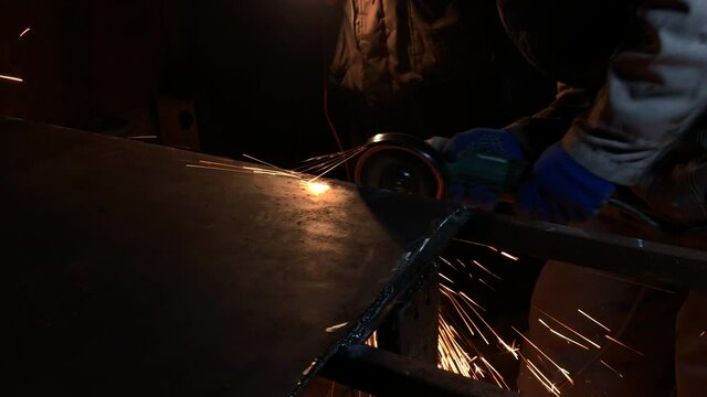 The process of electric grinding of metal metal. Bright flames and sparks. Master in work gloves.