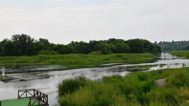 Inflated boats swim and rafting by river time lapse. Southern Bug river shore and rippled water overgrown by reeds and bulrush plants. Tranquil landscape of Bug Gard islands parkland in Ukraine