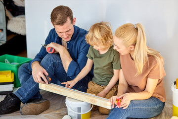 New life begins with home improvement. Family with kid boy repairing room together, sit on floor, explaining son what to do with repair tools and materials. Maintenance and repair, family lifestyle