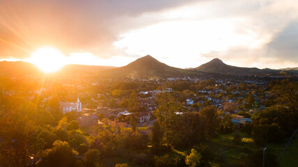 Beatific golden sunlight flooding over mountain range onto small town with white church with steeple