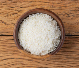 Grated coconut flakes in a bowl over wooden table