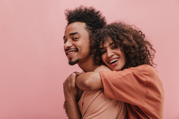 close-up studio shot of two charming partners on pink background. smiling curly brunette hugs...