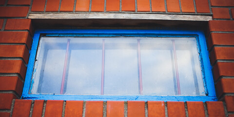 Low window with old blue frame and iron grating in a orange brick building