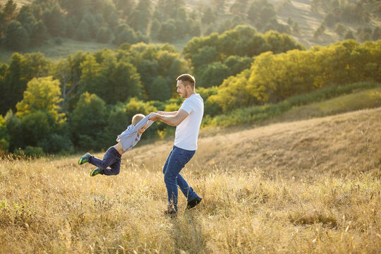 dad circles his son in the grass against the background of trees and bushes