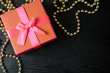 Closeup of red present box with pink ribbon and bow on the black wood