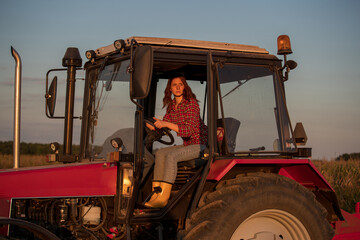 Young female farmer driving tractor in field at sundown.