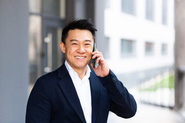 portrait Asian businessman talking on the phone cheerful smiling reports good news near the office center outside looking at the camera