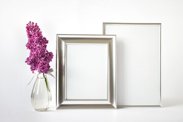 Mockup template with two blank silver frames and pink lilac flower branch in glass vase on white background.