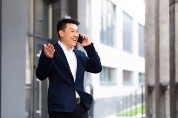 Asian businessman talking on the phone cheerful smiling reports good news near the office center...