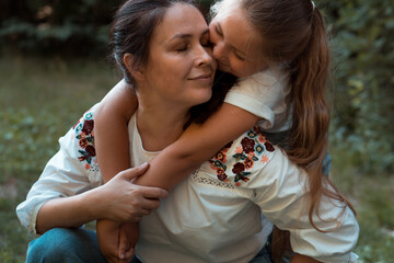 Adult woman and little girl (mother and her daughter) hugging in park or forest