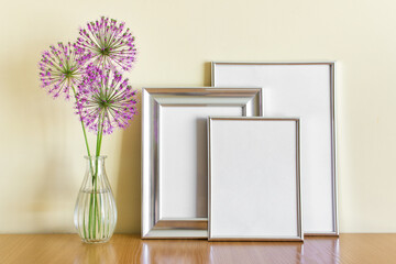 Mockup template with standing stack of silver frames and pink circular summer garlic flowers in glass vase.