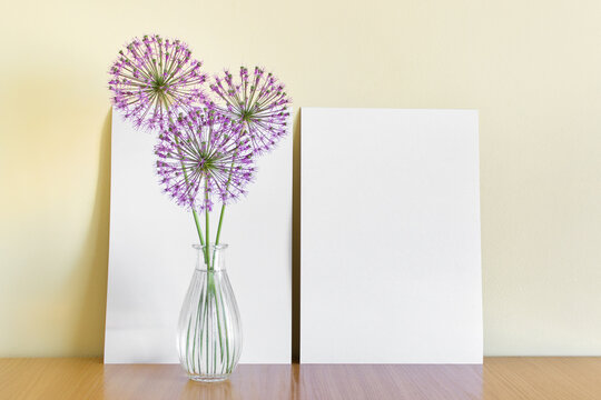 Mockup template with two A4 paper sheets standing next to yellow wall with circular garlic pink flowers in glass vase.