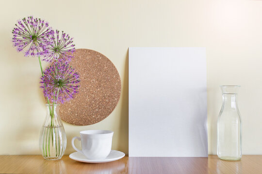 Mockup template with A4 paper sheet, porcelain cup, purple garlic flowers, corc circle and glass vases.