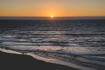 Fototapeta premium Panoramic view of the pacific ocean and beautiful sunset in the horizon with sun and rays in the center and the shore and beach with birds silhouettes