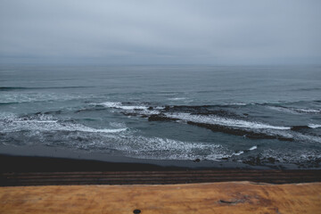 Rustic wood table and panoramic view of the pacific ocean with waves, the horizon with cloudy sky and the shore and beach