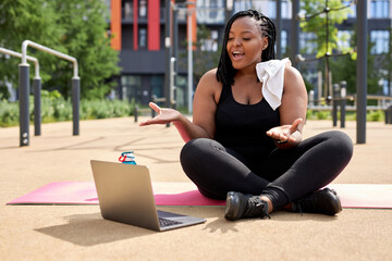 Smiling young overweight african woman talking with personal trainer instructor via video online on...