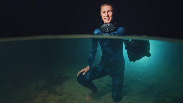 Underwater photographer in night lake. Portrait of the young woman in wetsuit holding underwater camera and standing in the lake at night