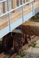 Close up of old rusted rail wheel on rails on a summer day. Grey painted handrails. Wood texture.