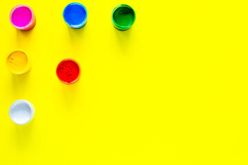 Cans of multi-colored paint are arranged in a triangle in the upper corner of the photo on a yellow background. top view, flat lay, copy space, isolate.