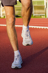 Fototapeta premium Close up young man runner athlete getting ready to run doing warm up and stretching exercises for muscles of legs before outside training to marathon on athletic field at sunrise time