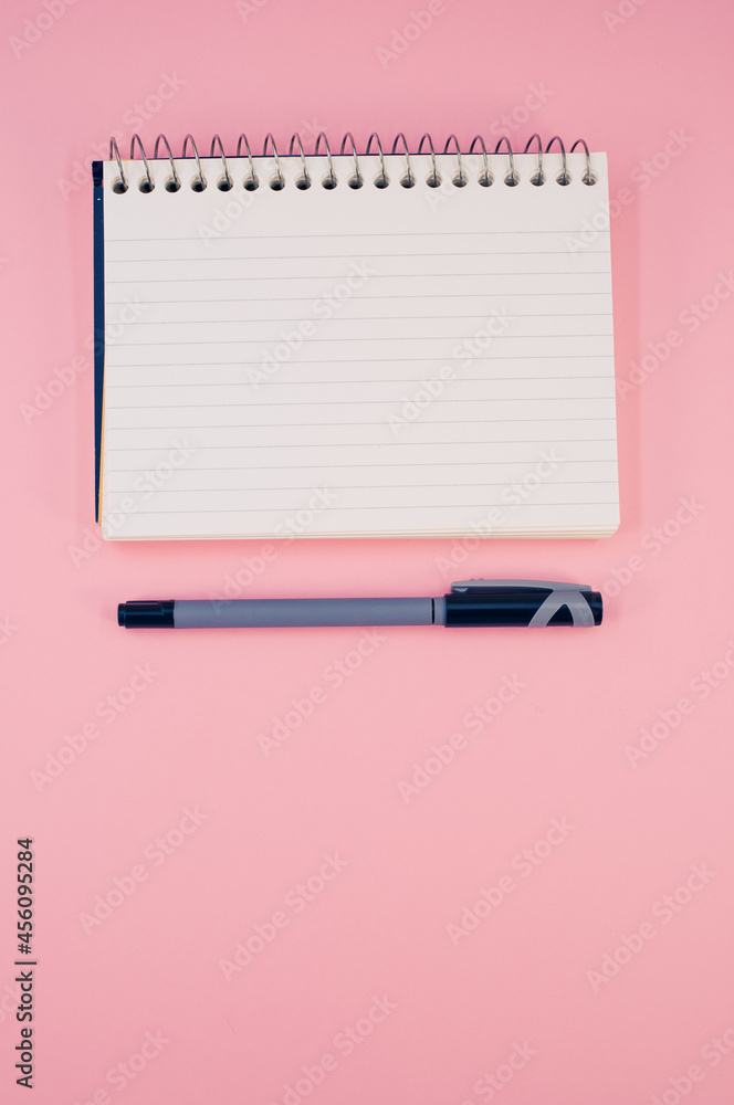 Poster vertical shot of an open notebook with a pen on a pink surface
