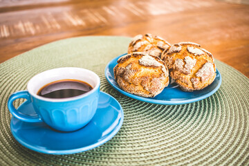 A cup of coffee and three brazilian corn breads on the table. 