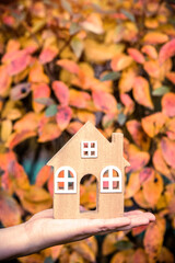 The symbol of the house in the girl's hand on the background of yellow leaves
