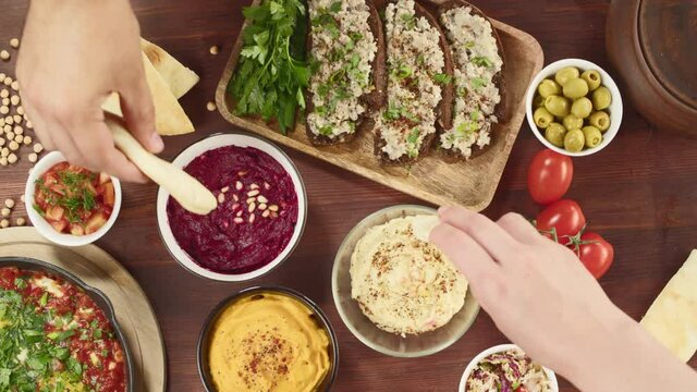 Israeli cuisine. Shakshuka in pan decorated with parsley, forshmak and hummus on table, eating pita with sauces. National Jewish dishes top view. Eggs fried in tomato sauce, middle eastern culture.