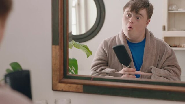 funny teenage boy with down syndrome dancing in bathroom having fun brushing hair enjoying morning routine getting ready wearing bathrobe