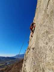 VERTICAL: Athletic male tourist rock climbing in Vipava scales a towering cliff.