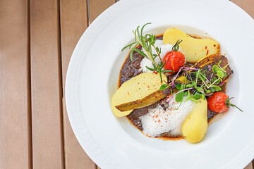 Beef stew with potatoes, tomatoes, roasted fennel and garnish of cress, herbs and sprouts, served with decorative foam on a white plate on a wooden table, copy space, high angle view from above