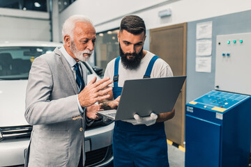 Car mechanic talking with senior business man costumer during periodic car condition check. Technical inspection.