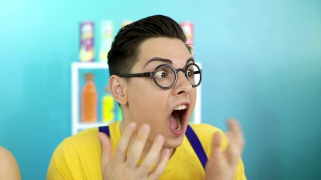 A young guy with glasses shouts for help. The man's mouth is burning with chili peppers. 